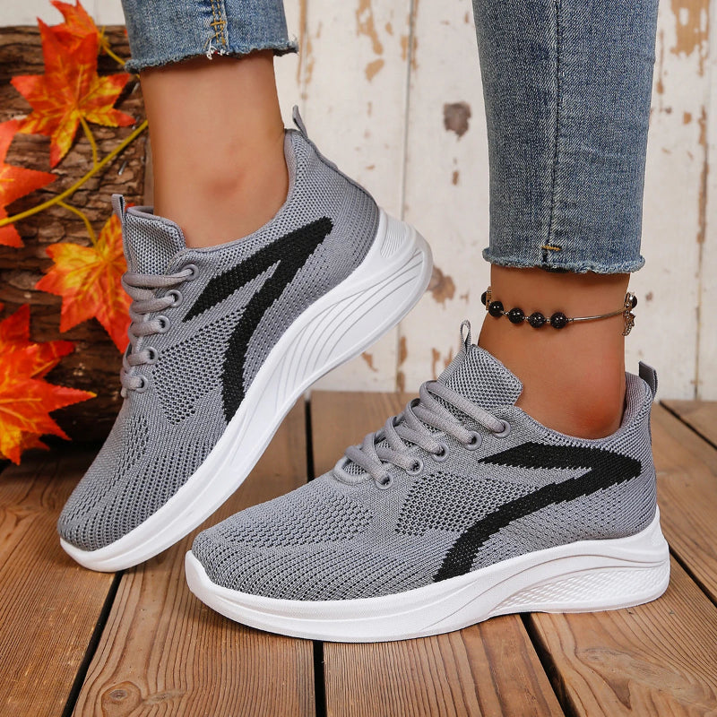 Gray running shoes with black accents worn by a person on a wooden floor.