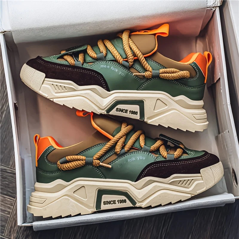 Pair of green and brown sneakers with orange laces in a box.