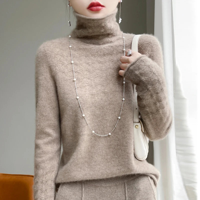 Person wearing a beige turtleneck sweater with a pearl necklace and white handbag.