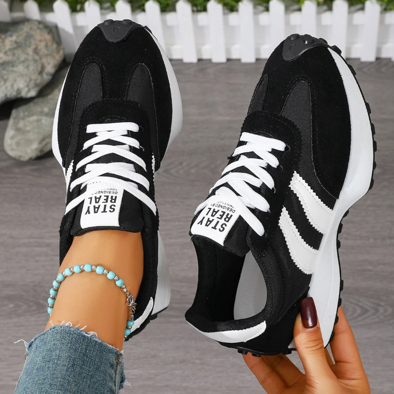 Black and white sneakers held by a person with a blurred background
