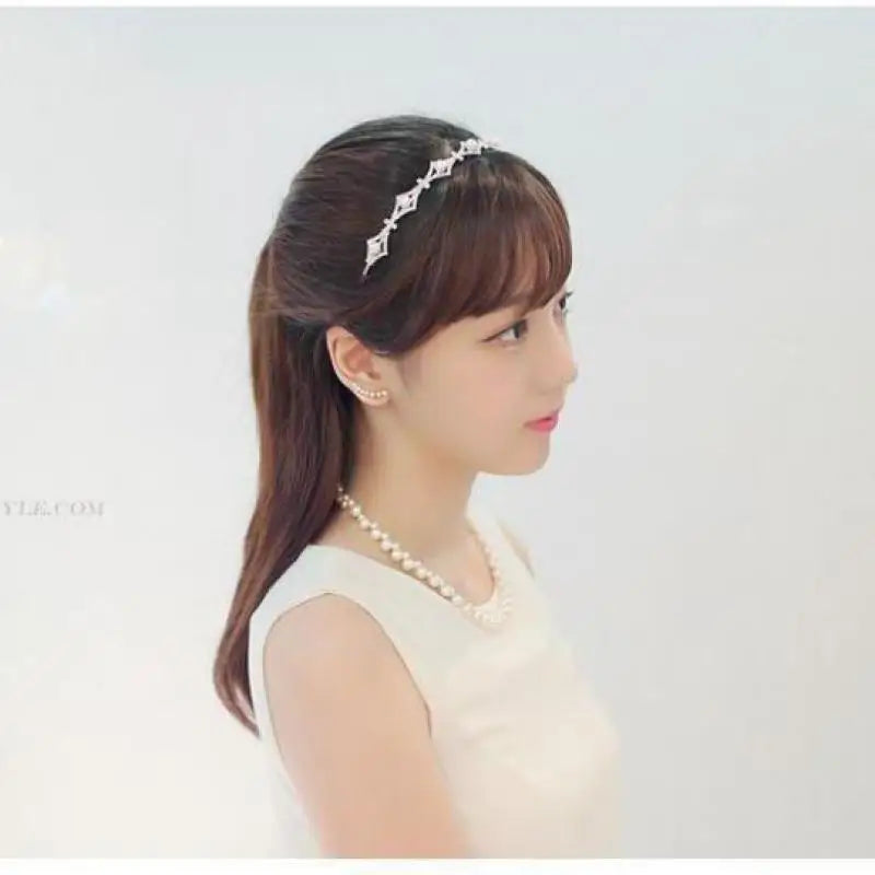 Woman with hair styled with a headband and pearl necklace against a plain background