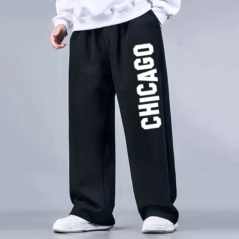 Black sweatpants with 'Chicago' printed on the side worn by a person against a gray background
