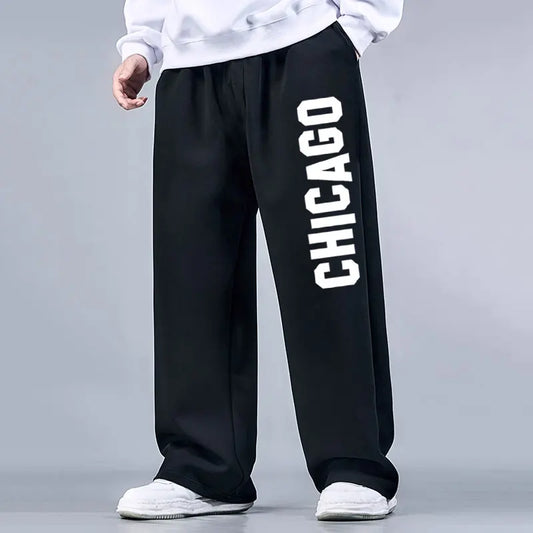 Black sweatpants with 'Chicago' printed on the side worn by a person against a gray background