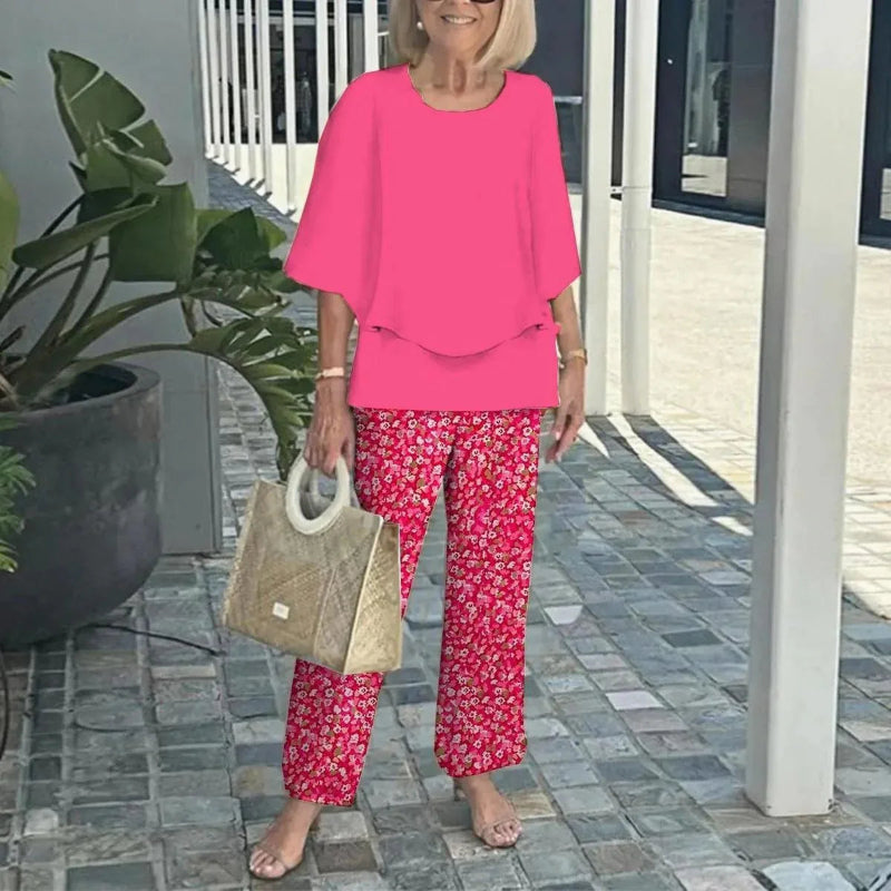 Woman in pink outfit with floral pants holding a beige bag outdoors.