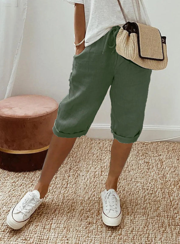 Person wearing green shorts, white sneakers, and a straw bag indoors.