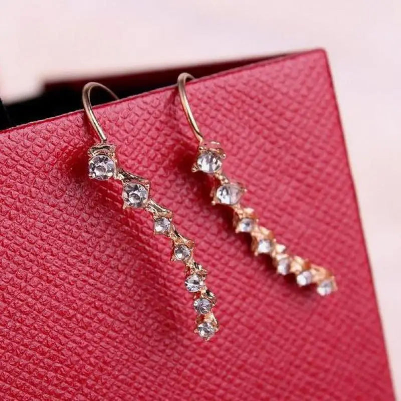 Gold earrings with clear stones on a red textured surface