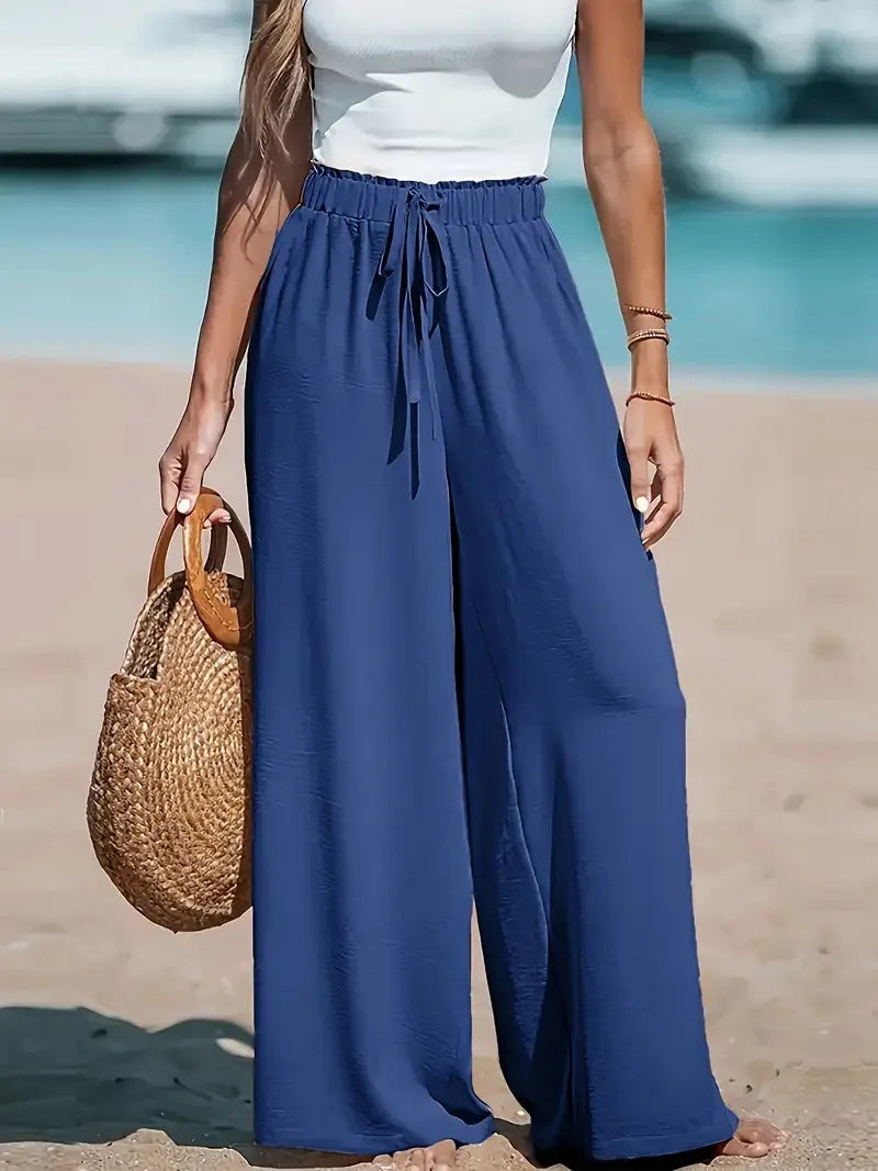Person wearing blue wide-leg pants and a white top on a beach.