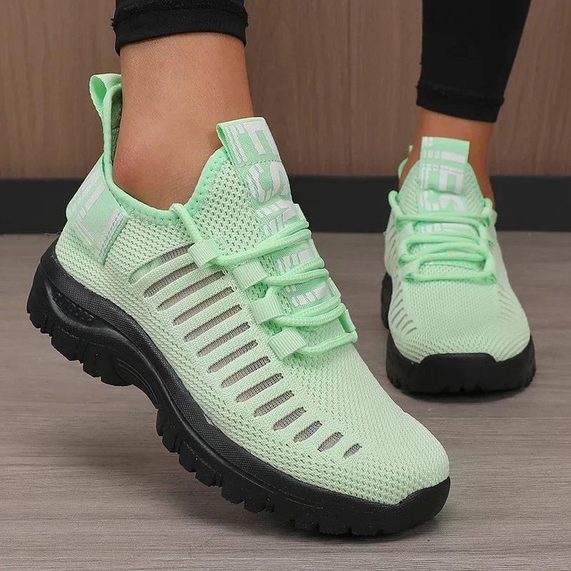 Light green sneakers with black soles worn by a person on a wooden floor.