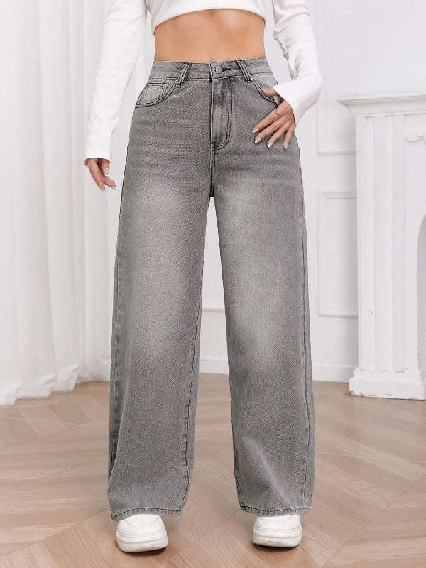 Person wearing gray wide-leg jeans and white sneakers in a minimalistic room.
