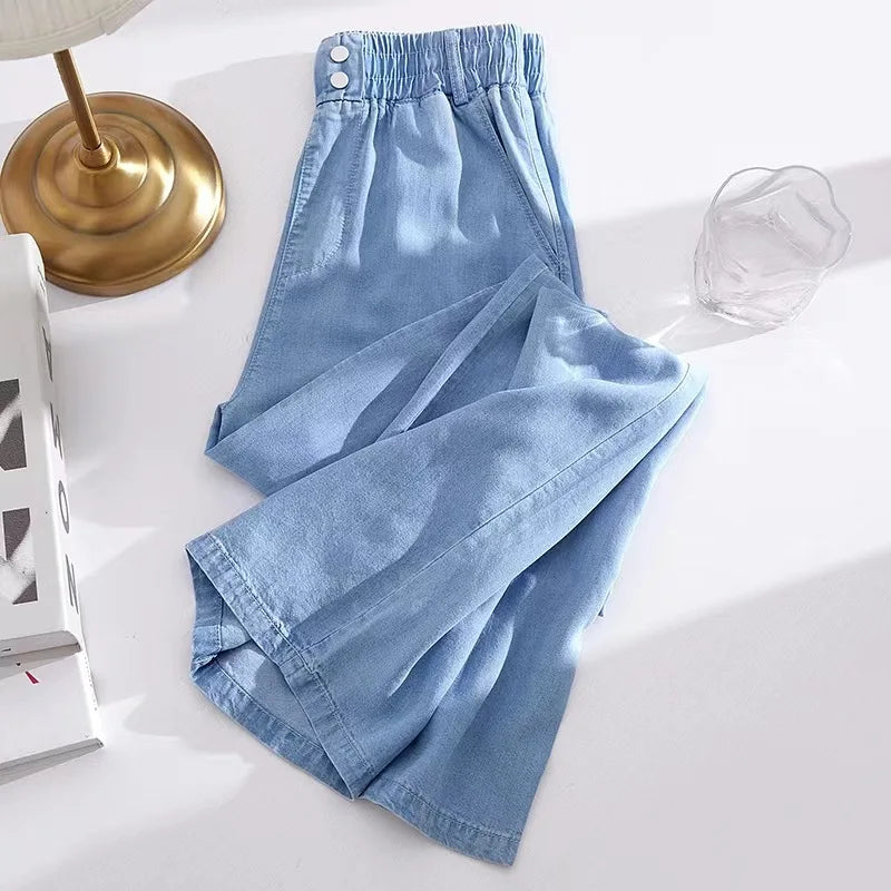 Light blue denim pants on a white surface with a lamp and glass in the background