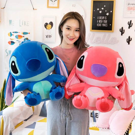 Woman holding two large plush toys, one blue and one pink, in a room with decorative elements.
