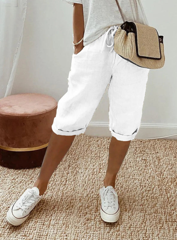 Person wearing white sneakers, white pants, and a straw bag indoors.