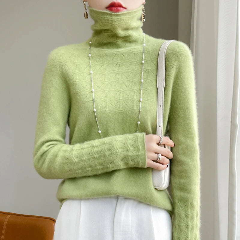 Person wearing a green turtleneck sweater holding a white handbag indoors.