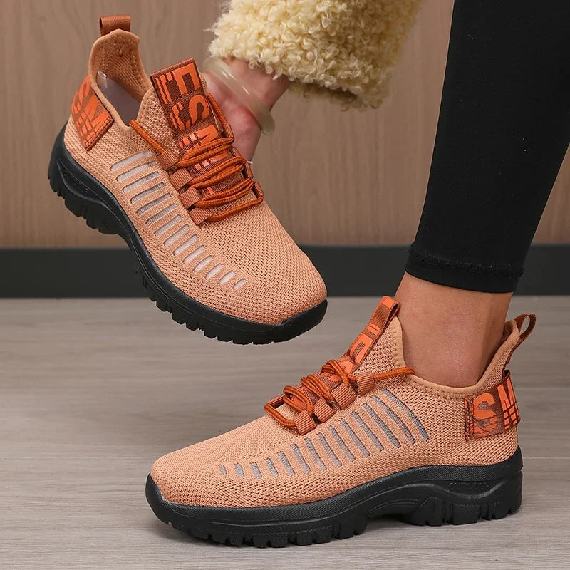Pair of orange and black shoes with a brand logo on a wooden floor.
