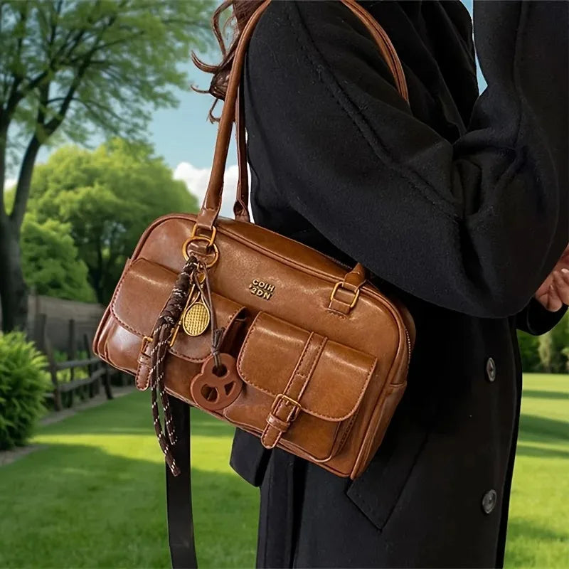 Brown leather bag with gold accents held by a person in a black coat outdoors.