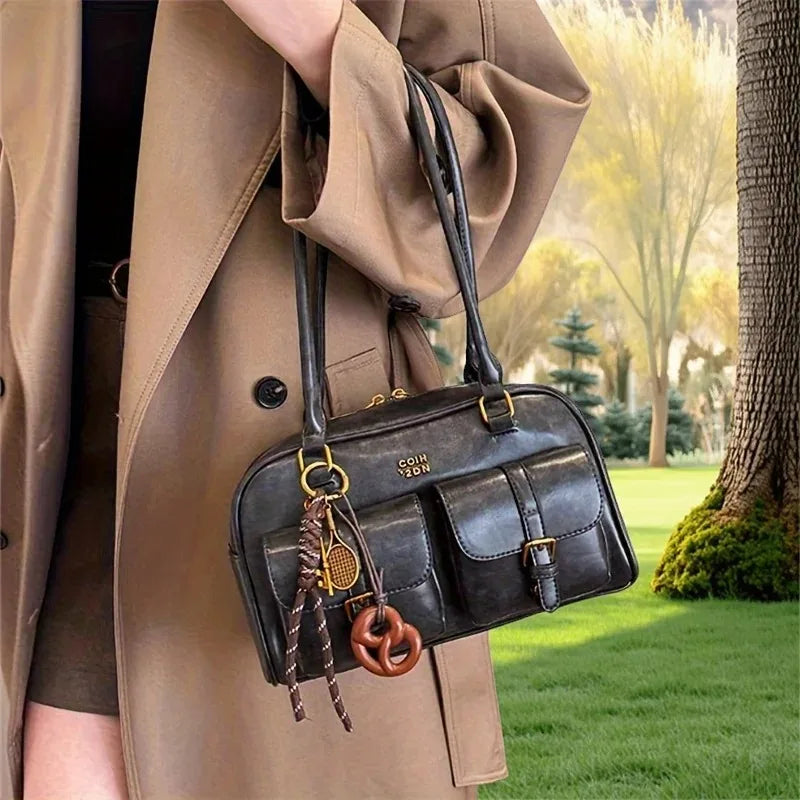 Person wearing a beige coat holding a black handbag with decorative elements in an outdoor setting.