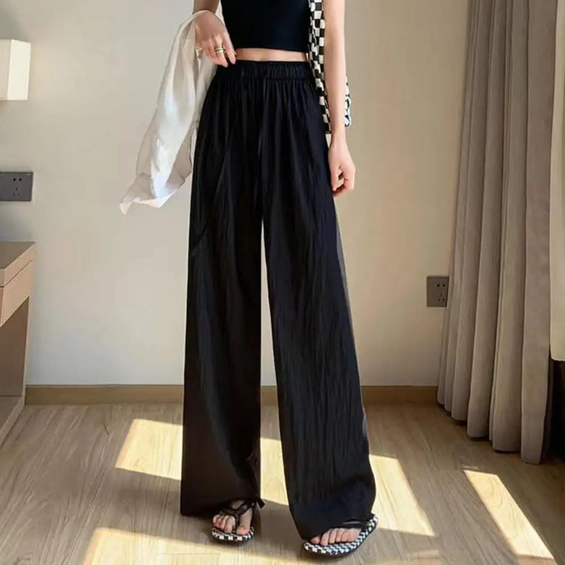 Person wearing black wide-leg pants in a room with wooden flooring and curtains.