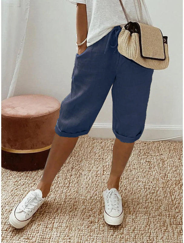 Person wearing blue shorts, white sneakers, and a straw bag indoors.