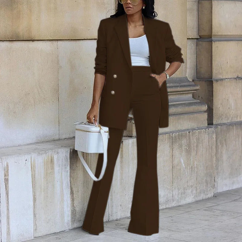 Woman in a brown suit standing against a stone wall.