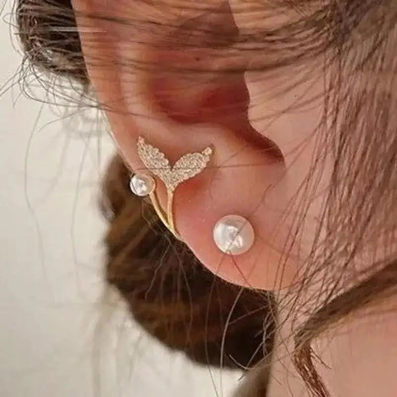 Close-up of an ear with gold and pearl earrings against a neutral background