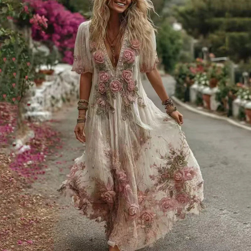 Woman in a floral dress walking on a path with flowers and greenery around.