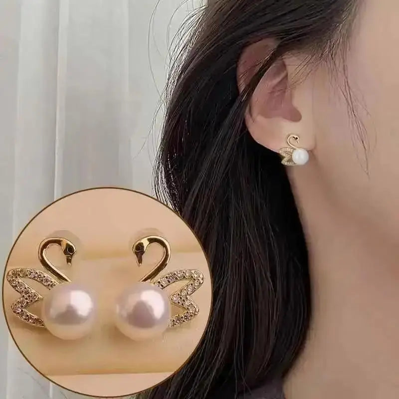 Pearl earrings with gold Swan design worn by a person, close-up on ear.