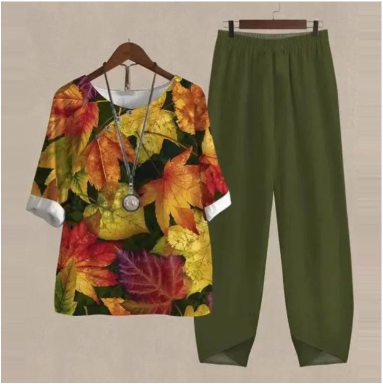 Colorful leaf-patterned top and green pants on hangers against a beige background