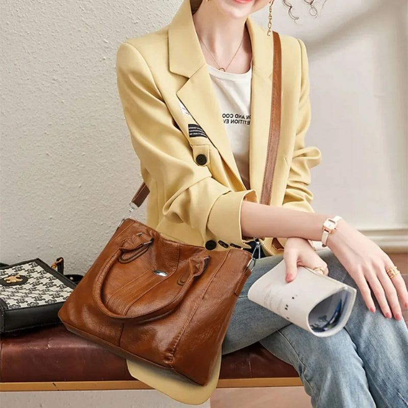 Person wearing a beige blazer with a brown leather handbag sitting on a bench.