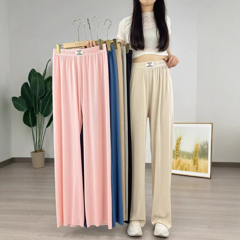 Woman holding up four pairs of colorful pants on hangers against a plain background.