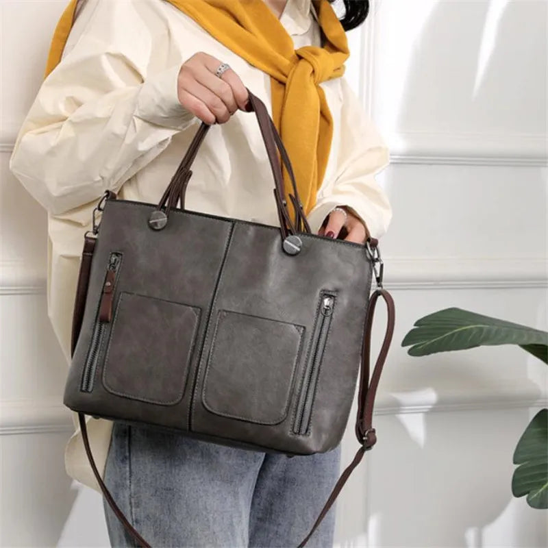Person holding a gray handbag with brown straps against a white wall.
