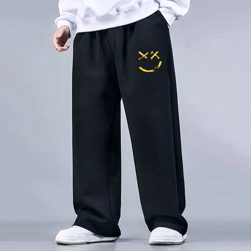 Black sweatpants with a yellow smiley face design on a gray background