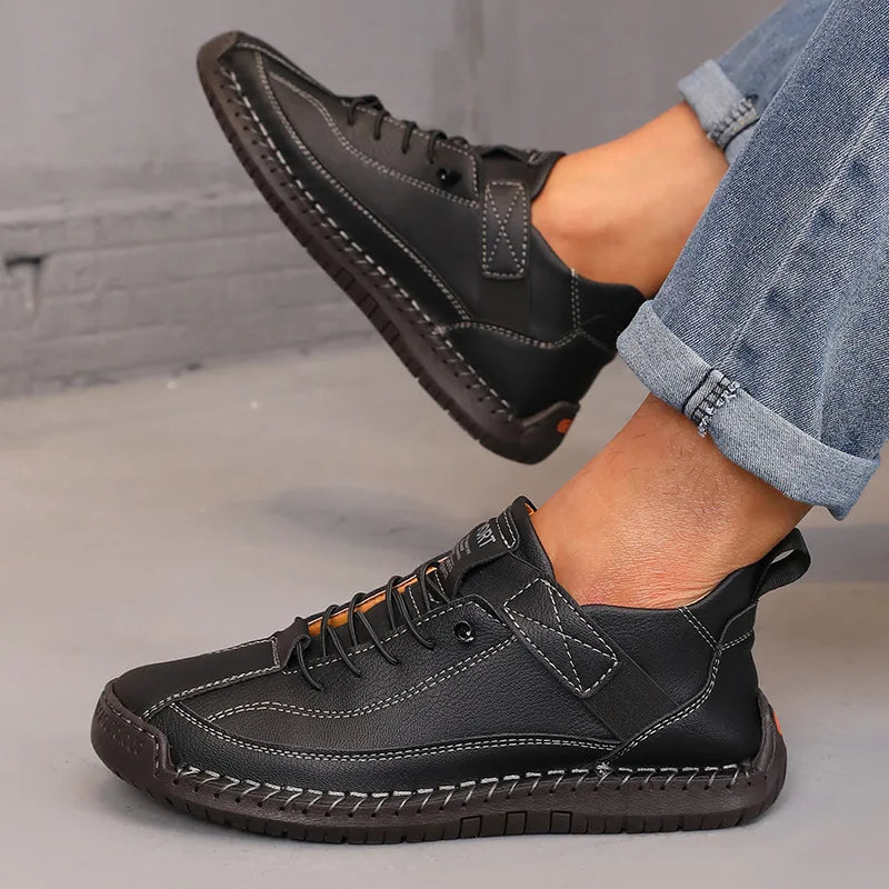 Black leather shoes worn with rolled-up jeans on a gray floor.