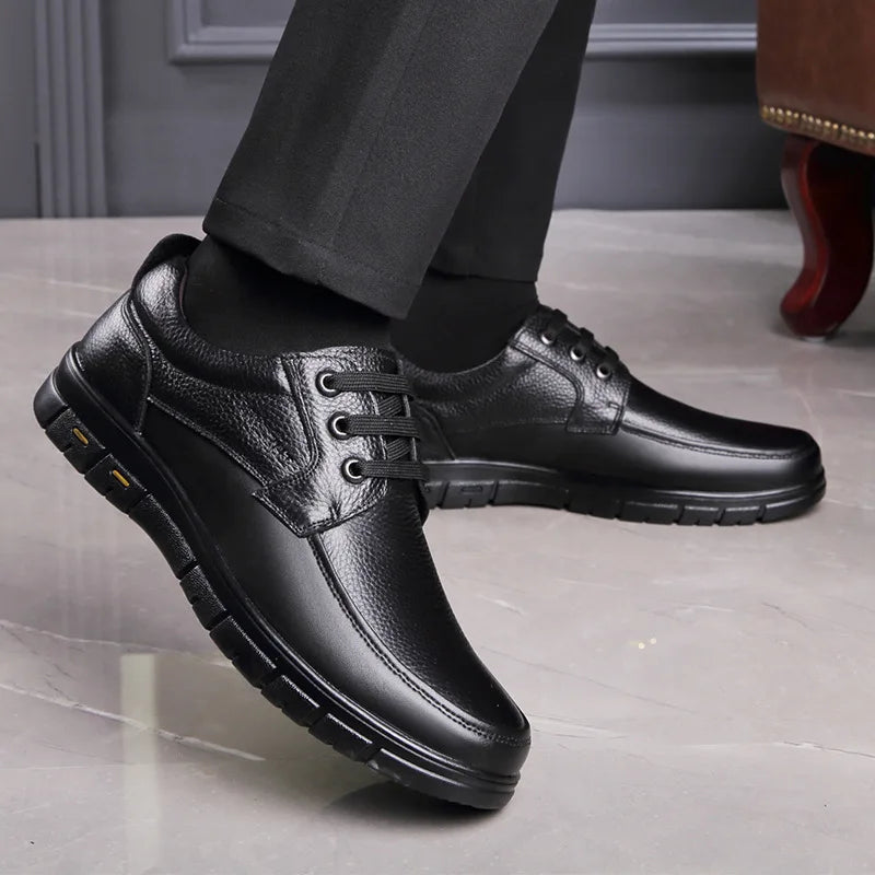 Black leather shoes worn with dark pants on a light wooden floor.