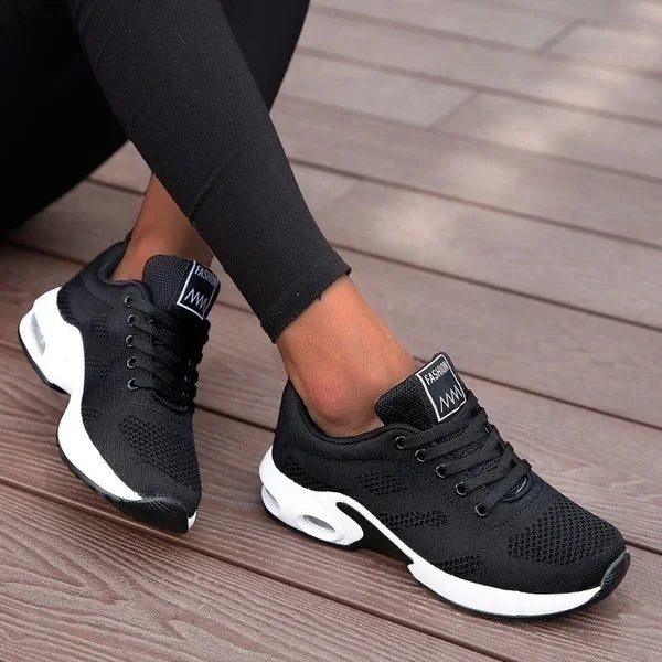 Black athletic shoes with white soles worn on a wooden floor