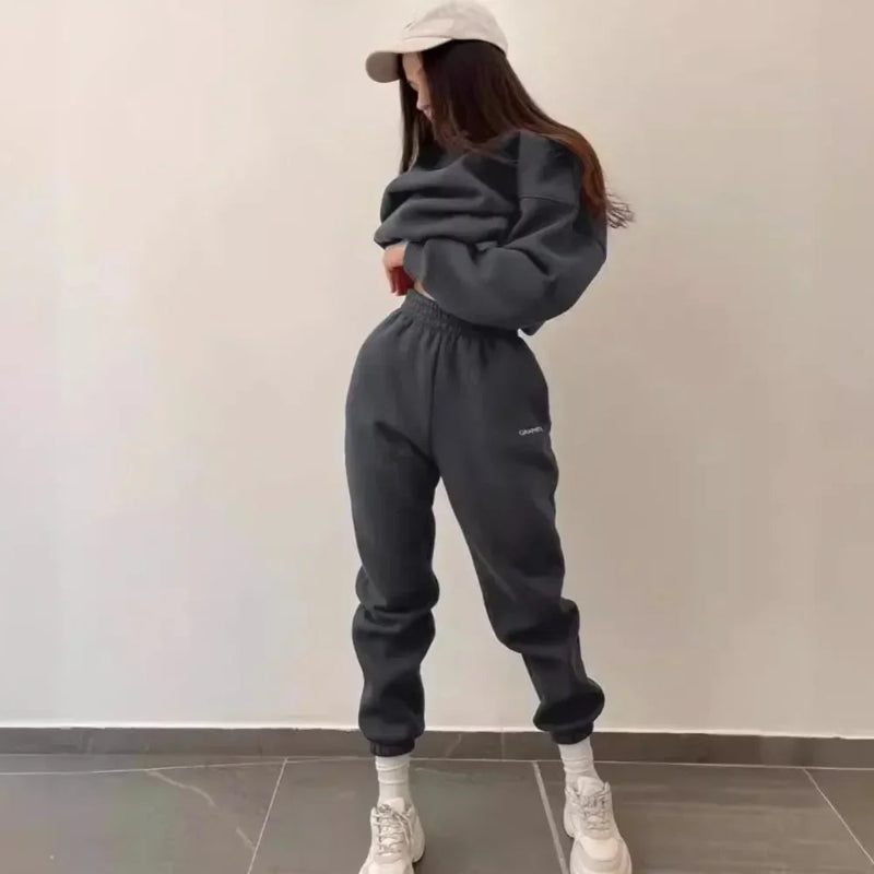 Person wearing a dark gray sweatshirt and pants with white sneakers against a plain background