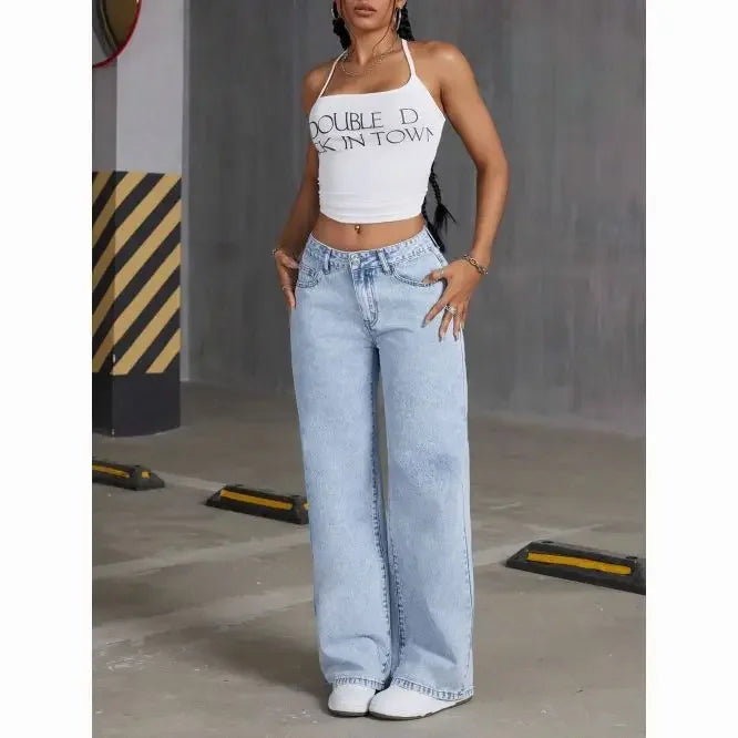 Person wearing a white crop top with text and light blue jeans in an urban setting.