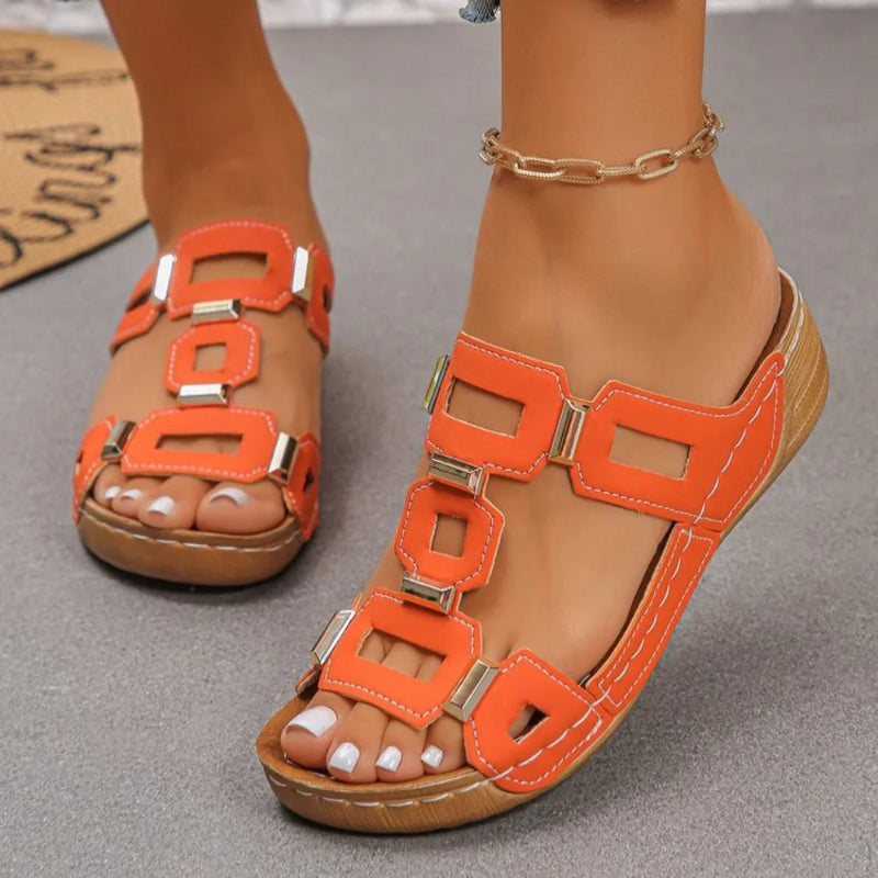 Orange sandals with brown soles worn by a person on a gray surface.
