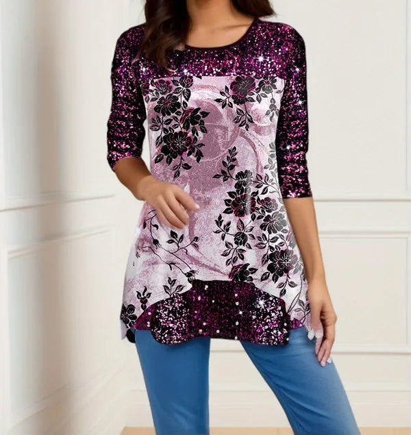 Woman wearing a floral and sequin top with blue pants against a white wall.