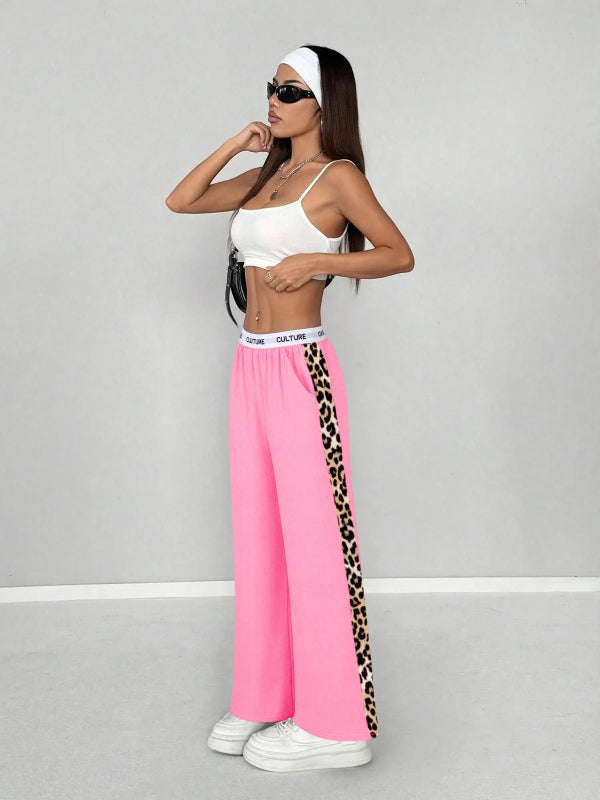 Woman wearing a white sports bra and pink pants with leopard print side stripes on a gray background