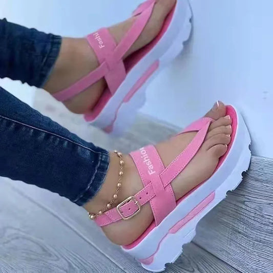 Pink sandals with white soles worn by a person on a light wooden floor.