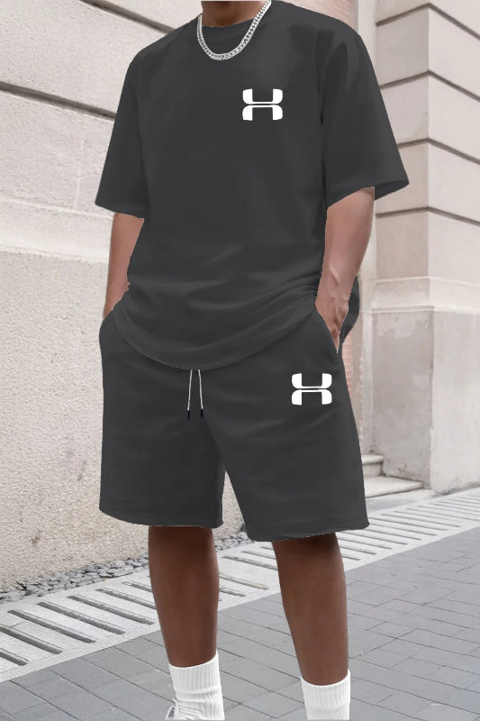 Person wearing black Under Armour t-shirt and shorts with a white logo, standing against a stone wall.