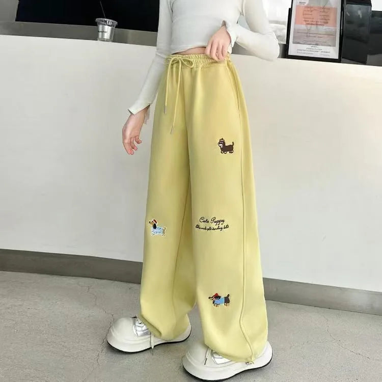 Person wearing light yellow sweatpants with embroidered designs indoors.