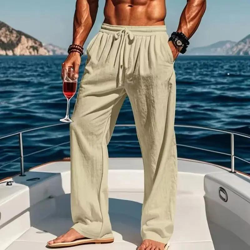 Man in light-colored pants holding a glass of red wine on a boat with ocean and mountains in the background