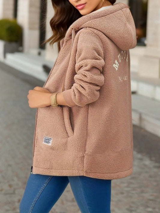 Person wearing a brown fleece jacket with brand logo, standing outdoors.