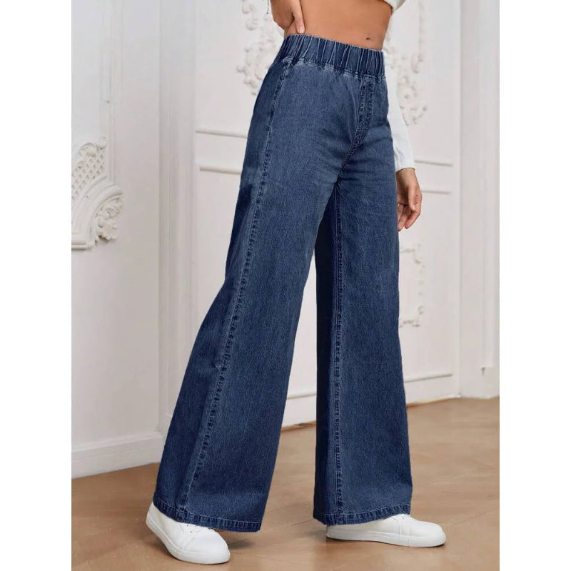 Person wearing blue wide-leg jeans and white sneakers in a minimalistic setting.