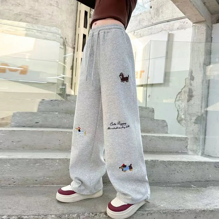 Person wearing gray sweatpants with embroidered designs on a staircase.