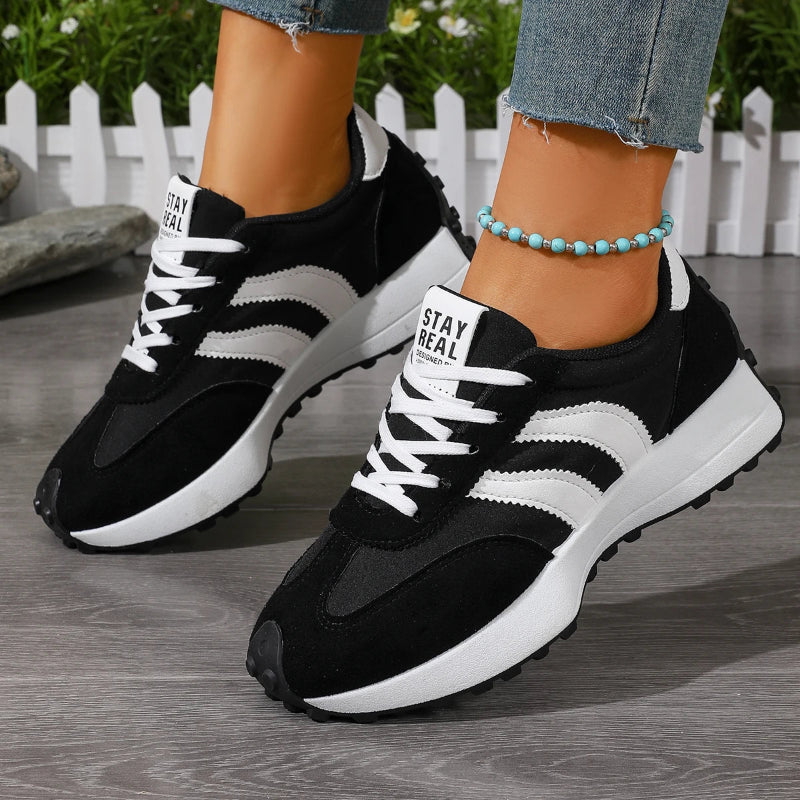 Black and white sneakers with 'Stay Real' text on a wooden floor.
