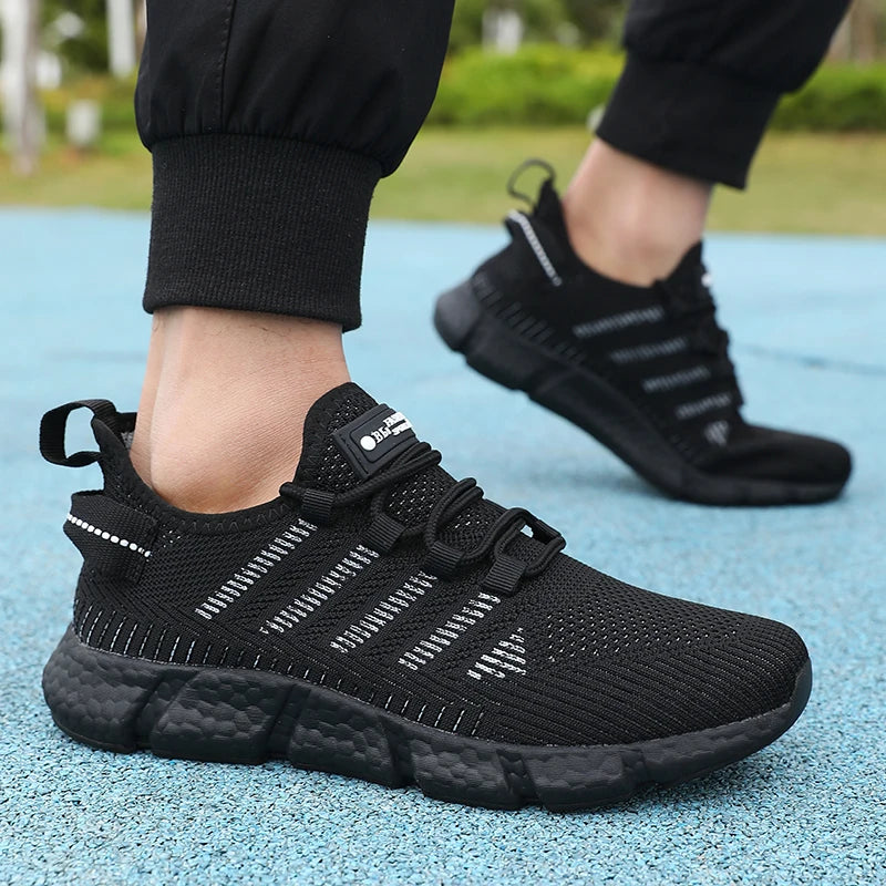 Black athletic shoes worn on a blue surface with blurred greenery in the background