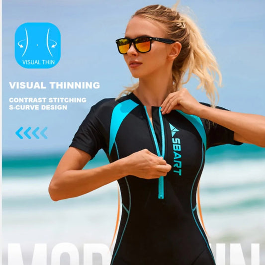 Woman wearing a black and blue swimsuit with sunglasses, standing against a beach background.