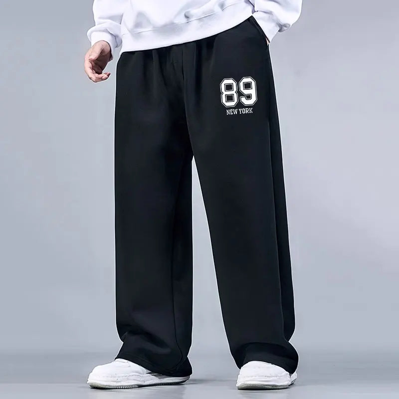 Black sweatpants with '89 New York' text worn by a person on a gray background